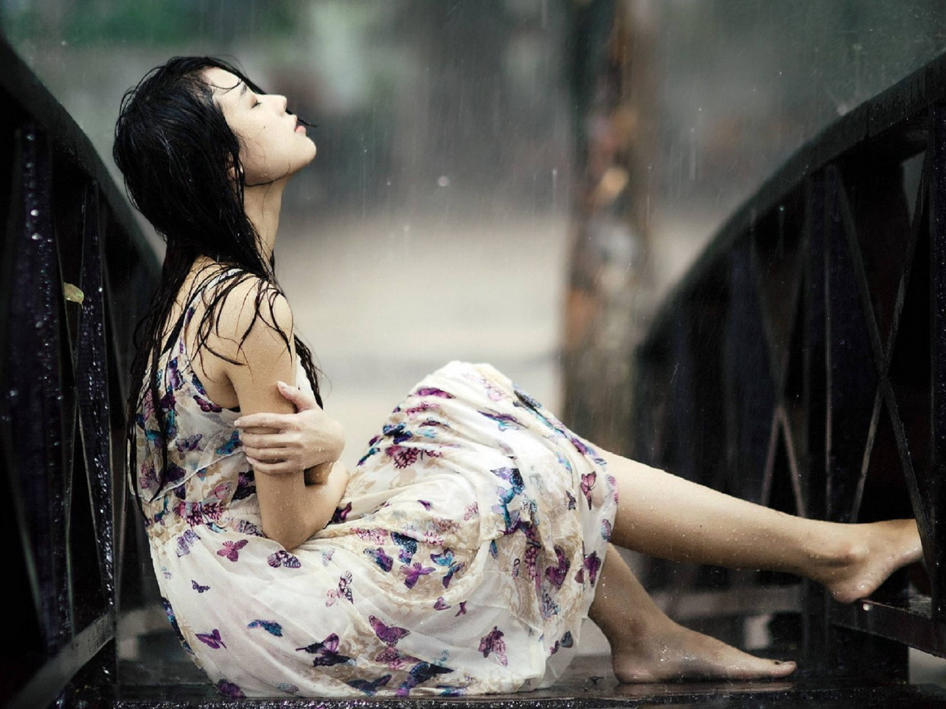 穿蝴蝶裙女子雨中坐在濕橋欄杆上