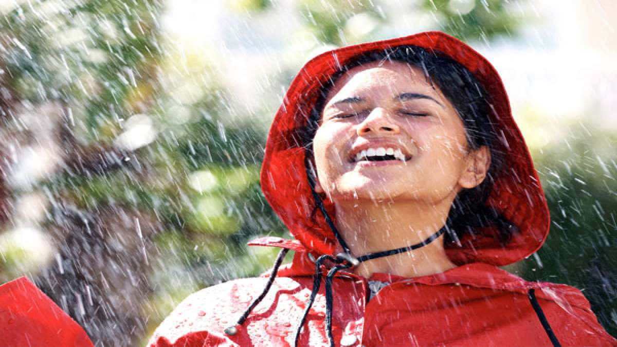 穿紅色雨衣的女人在雨中閉著眼睛笑。