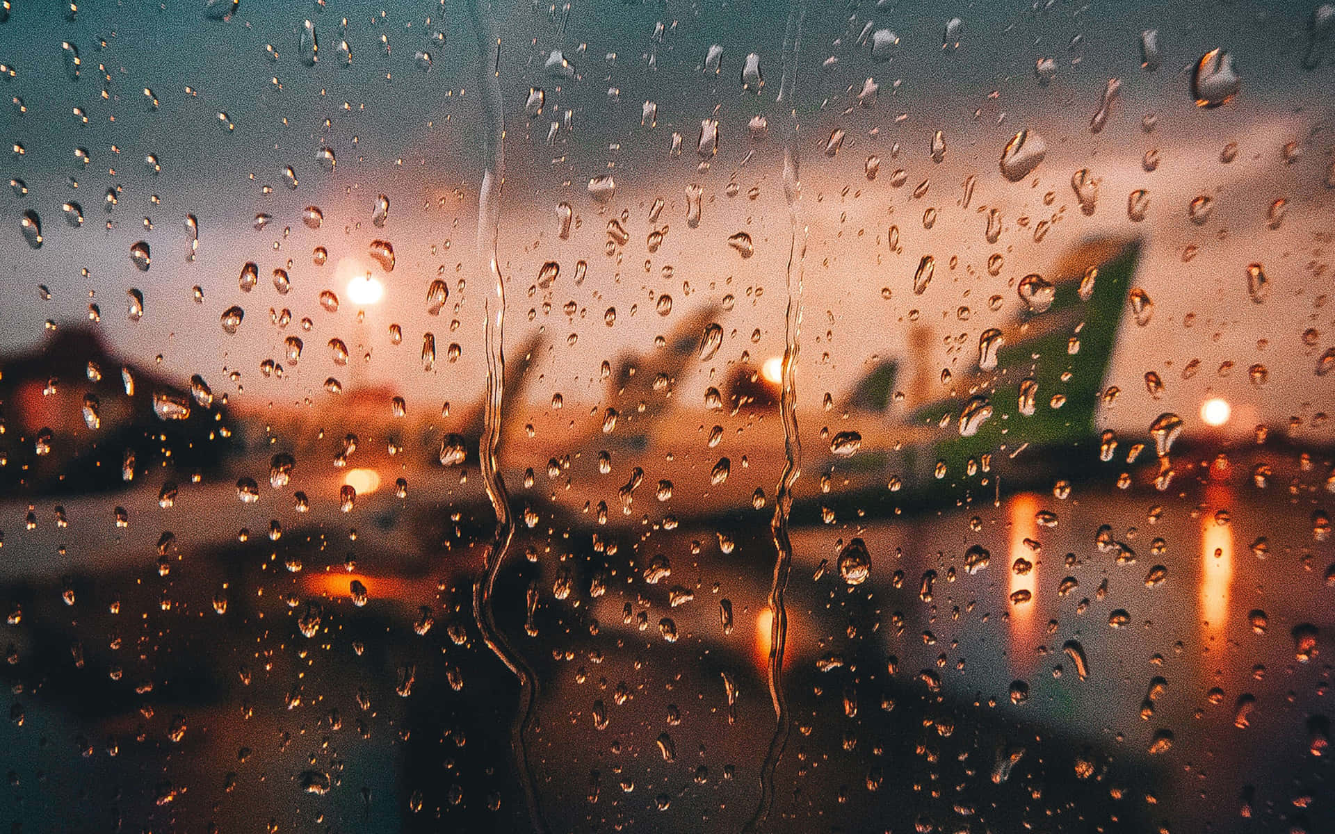 窗戶上的雨滴與模糊的機場飛機，暮色中