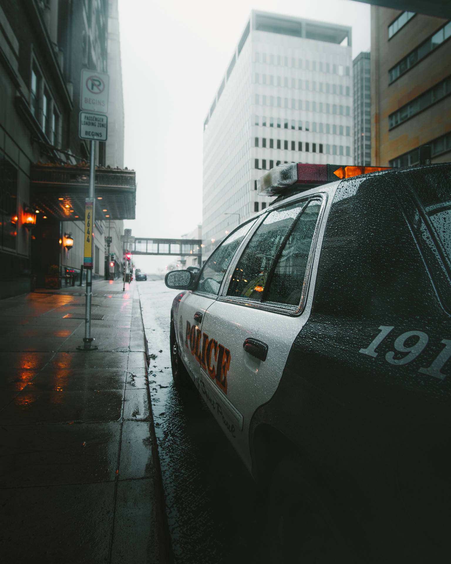 警車停泊在黃昏時分濕漉漉的城市街道上，車窗上有雨滴。