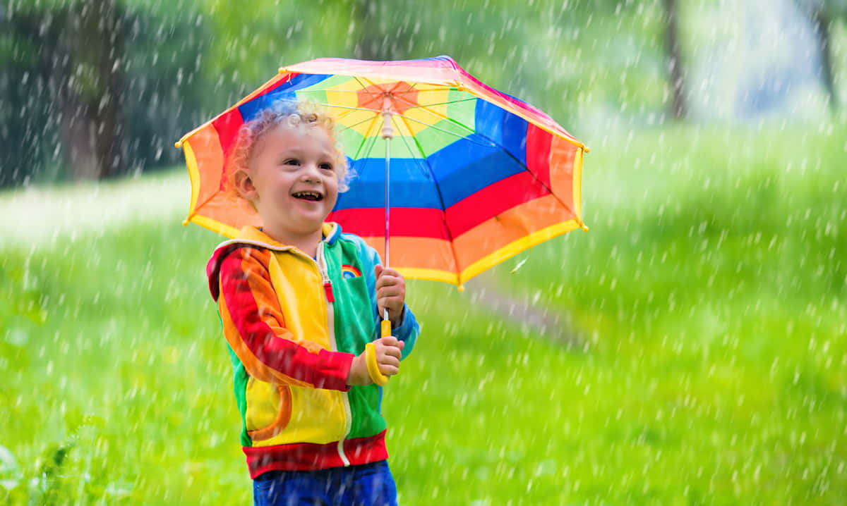 孩子拿著彩虹傘在雨中草地上大笑