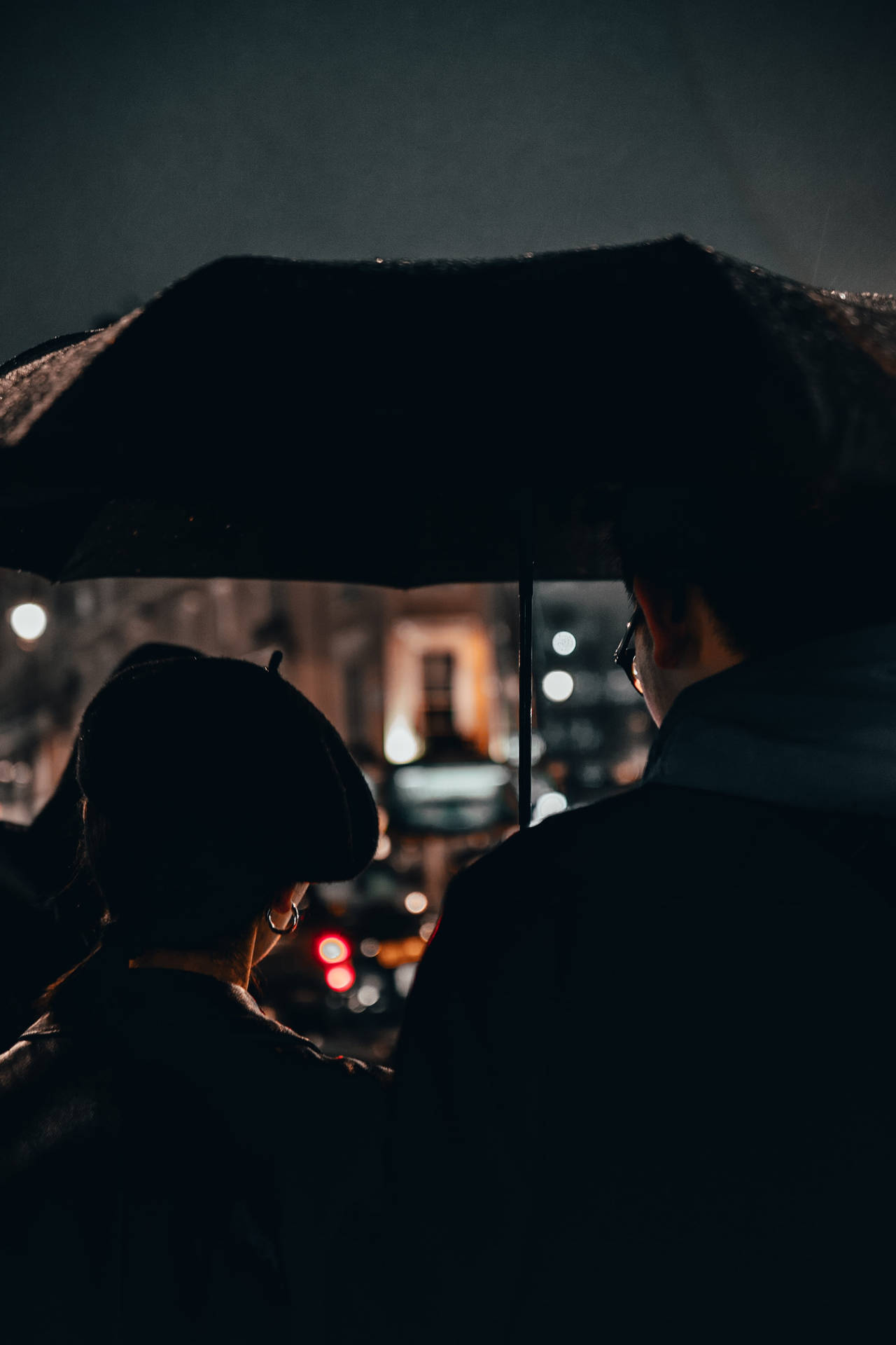兩人在夜間雨中共享一把雨傘，背後有城市燈光。