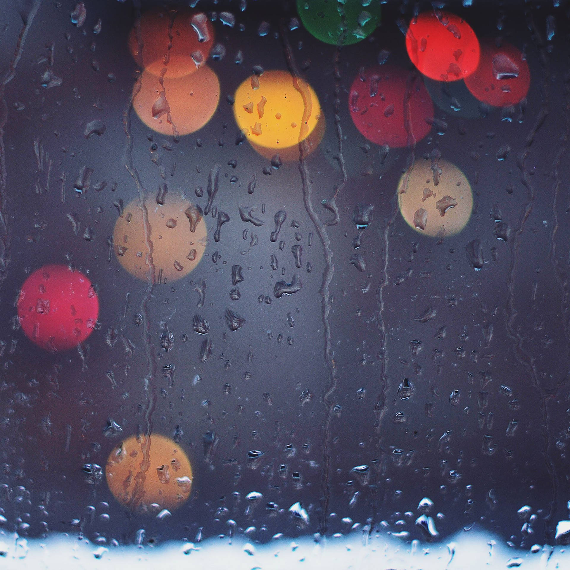 雨中散景 iPad mini 壁紙 — 雨滴沿窗戶流下，顯露出黑暗夜色中模糊多彩的城市燈光。