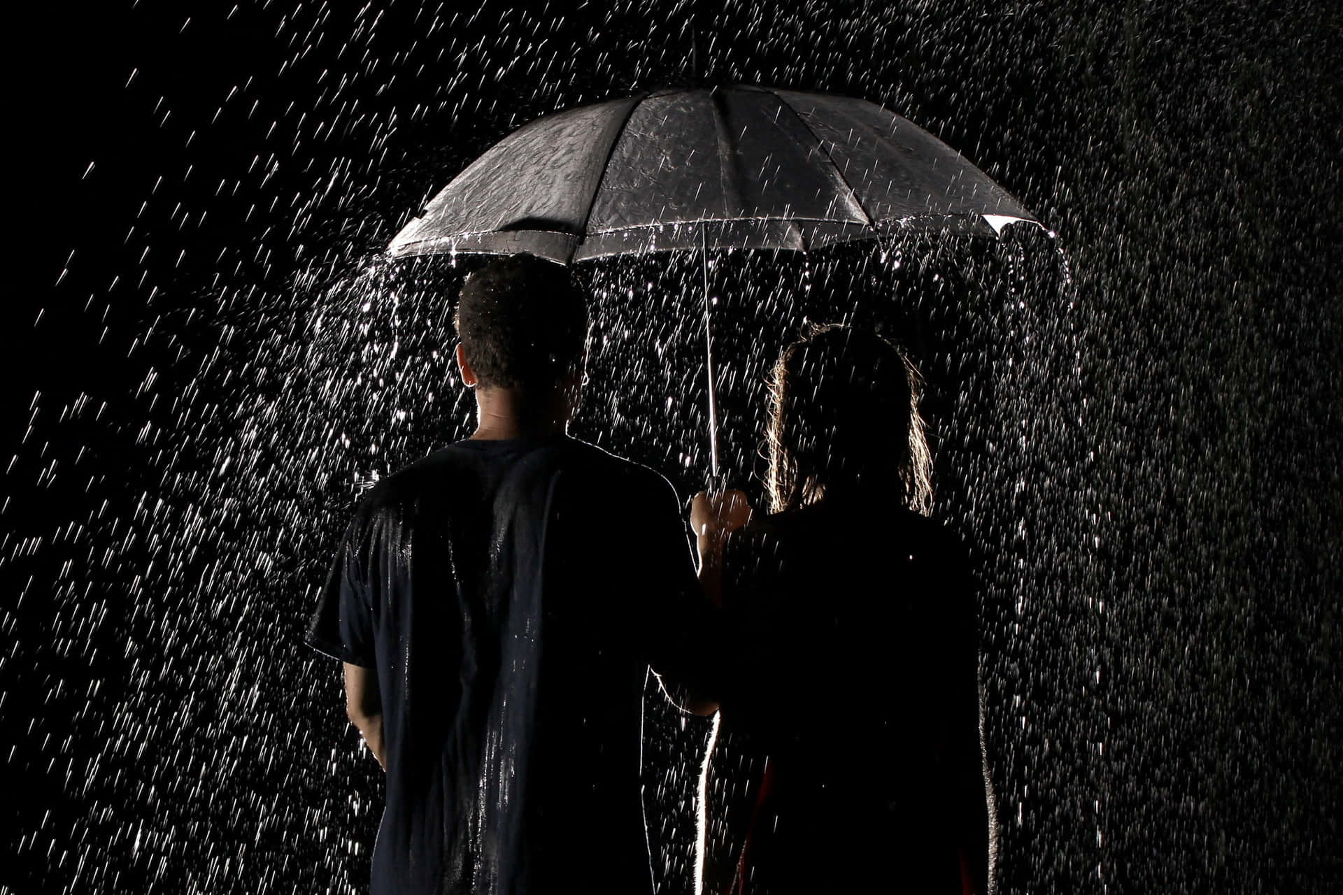 雨中浪漫情侶 壁紙 — 兩個剪影人物共用一把雨傘，雨水在漆黑背景中傾瀉而下。