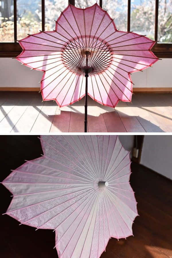 雨中漫步，一把雨傘為你撐起晴空 壁紙 — 一把精緻的粉紅色櫻花傘在室內打開，在木地板上投下柔和陰影，第二個視角展示其半透明面板和精緻框架。
