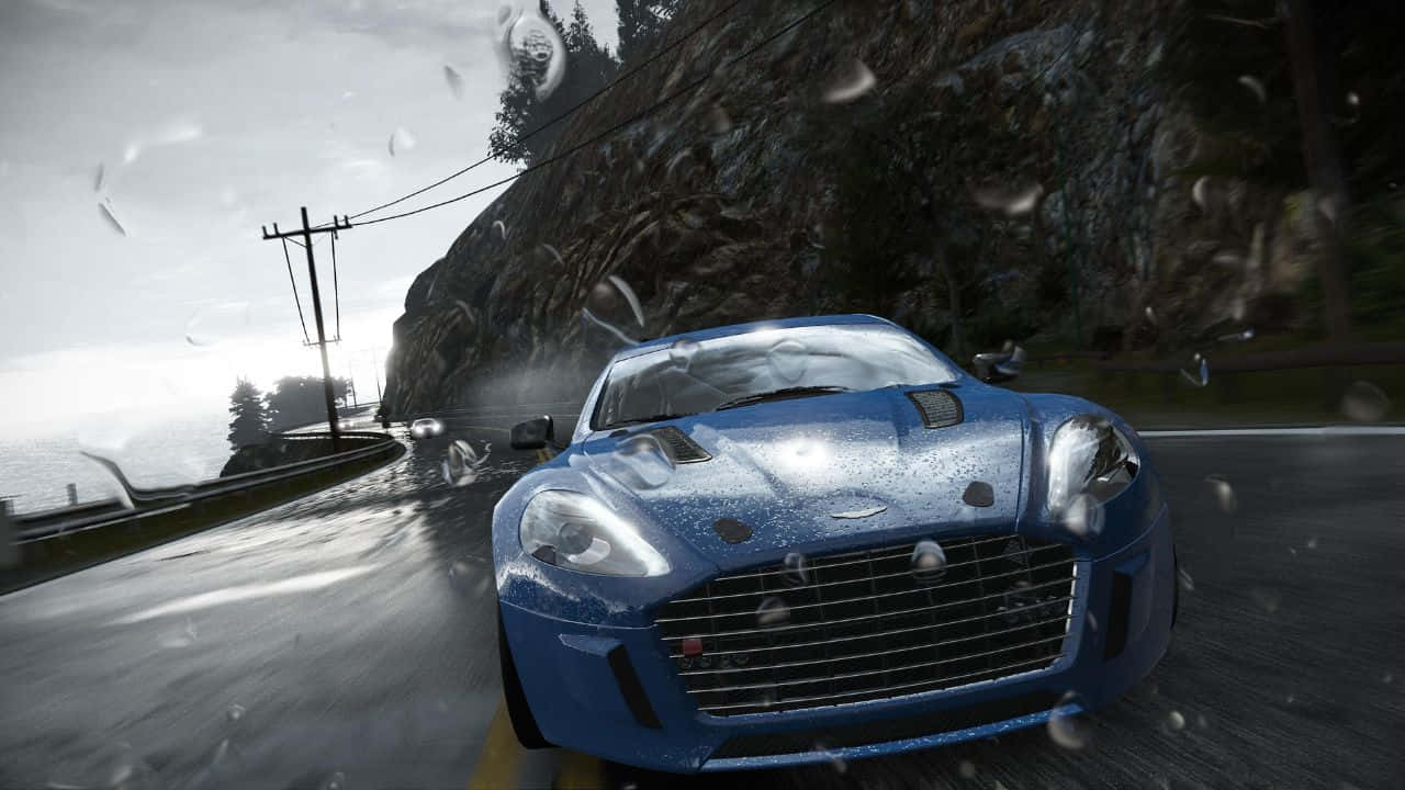 雨中濕潤 720p 項目賽車背景 壁紙 — 一輛藍色跑車在濕滑的海岸公路上飛馳，擋風玻璃上濺滿雨點，背景是霧氣朦朧的懸崖。