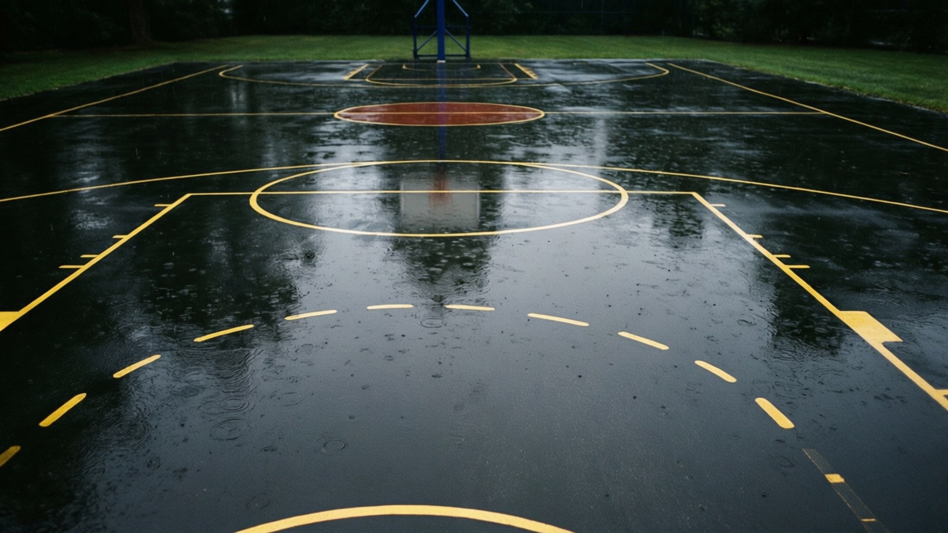 濕漉漉的籃球場，黃色線條在雨中反射樹木。
