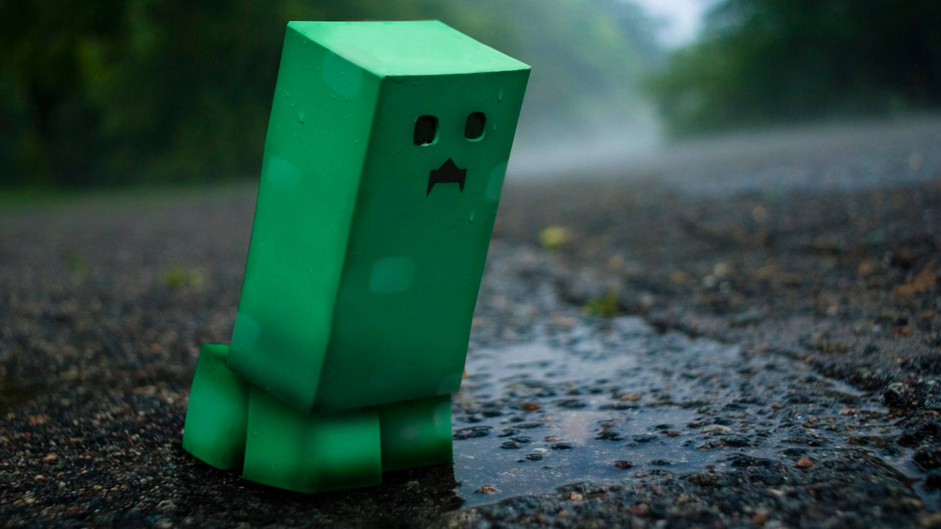 雨中的苦力怕 壁紙 — 一個綠色方塊狀的爬行者獨自站在潮濕的瀝青路上，天空多雲有霧。