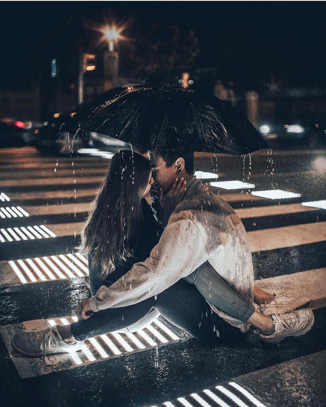 雨中相擁的兩位戀人 壁紙 — 一對情侶在夜間濕漉漉的城市行人過路處，於黑色雨傘下親密接吻，雨正下着。