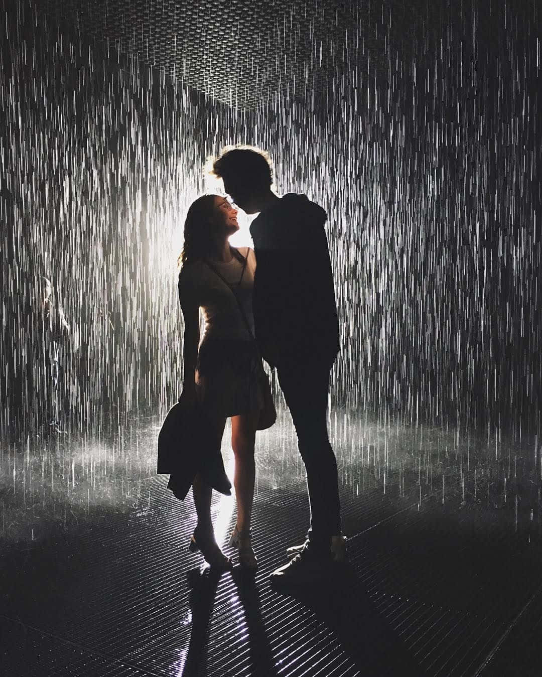 雨中緊握愛意 壁紙 — 一對剪影情侶在戲劇性的室內雨淋花灑下擁抱，帶有背光效果。