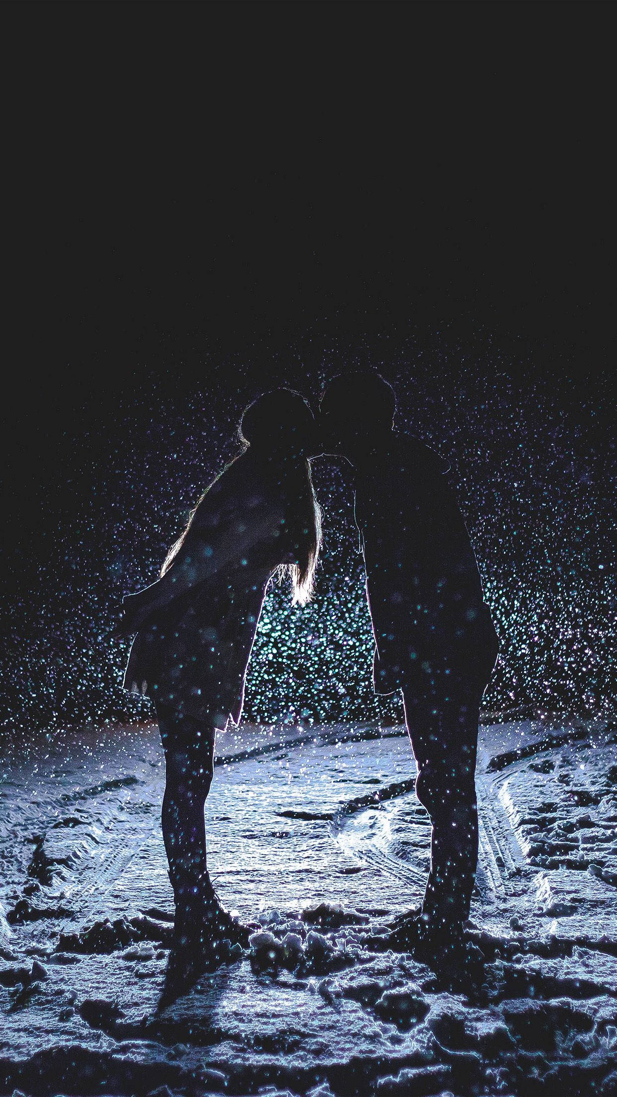 雨中親吻的愛情故事 壁紙 — 剪影情侶在黑暗的冬夜中，於飄雪下親吻，周圍有發光的粒子。