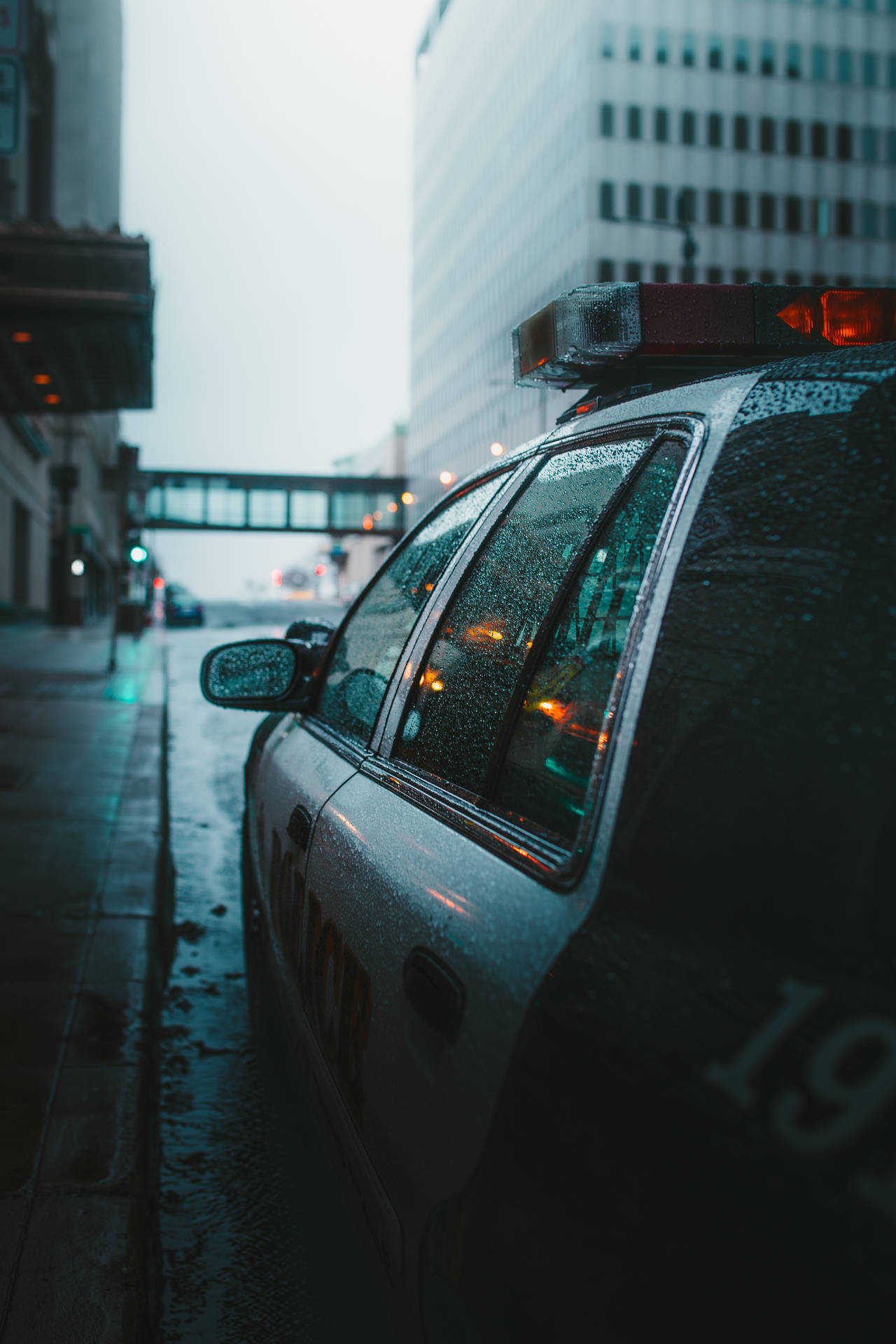 警車停泊在濕漉漉的城市街道上，夜晚，車窗上有雨滴。