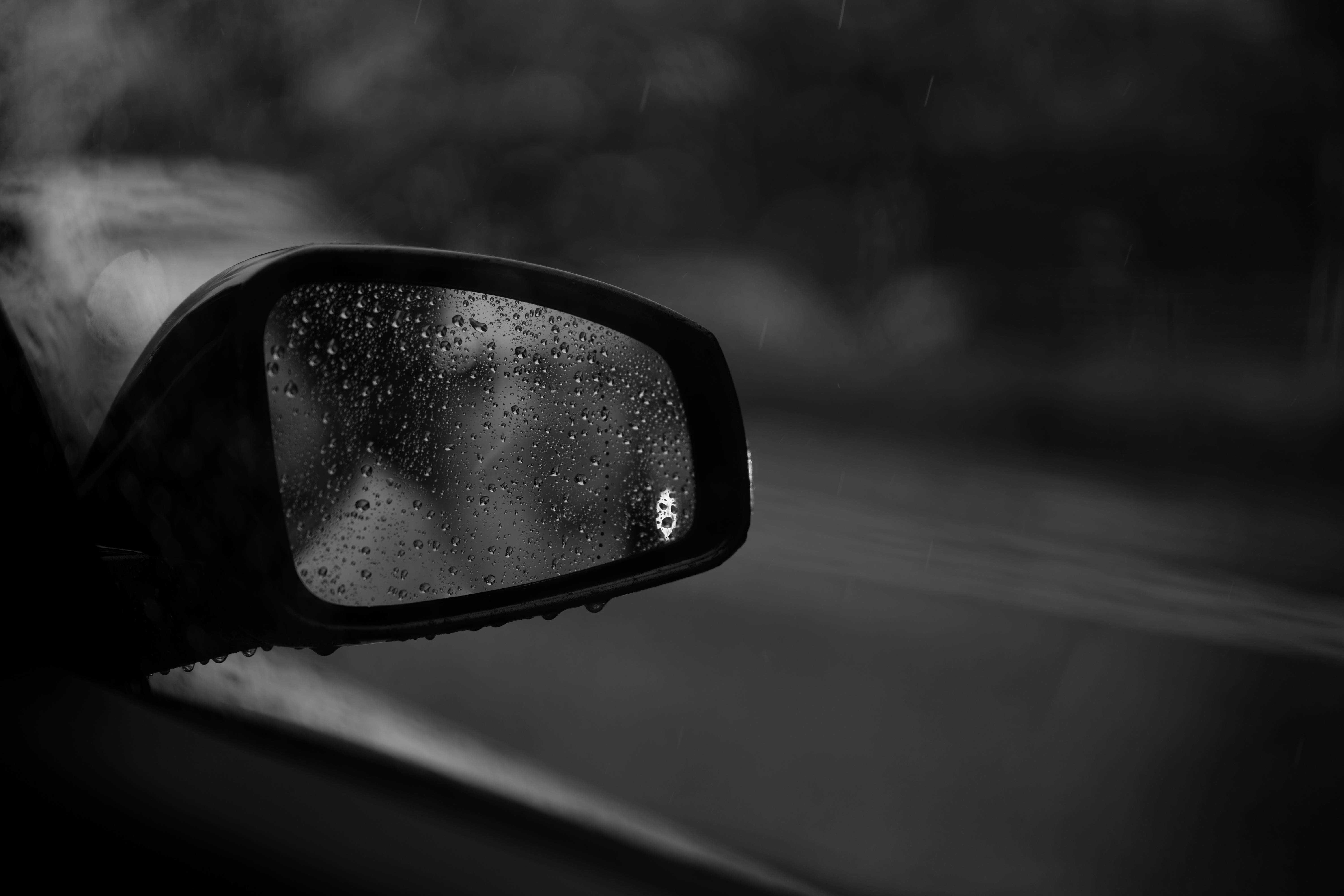 雨中車側後視鏡黑白壁紙 壁紙 — 一幅黑白特寫，展示沾滿雨點的汽車側鏡，在濕滑路面上反射出模糊的動態。