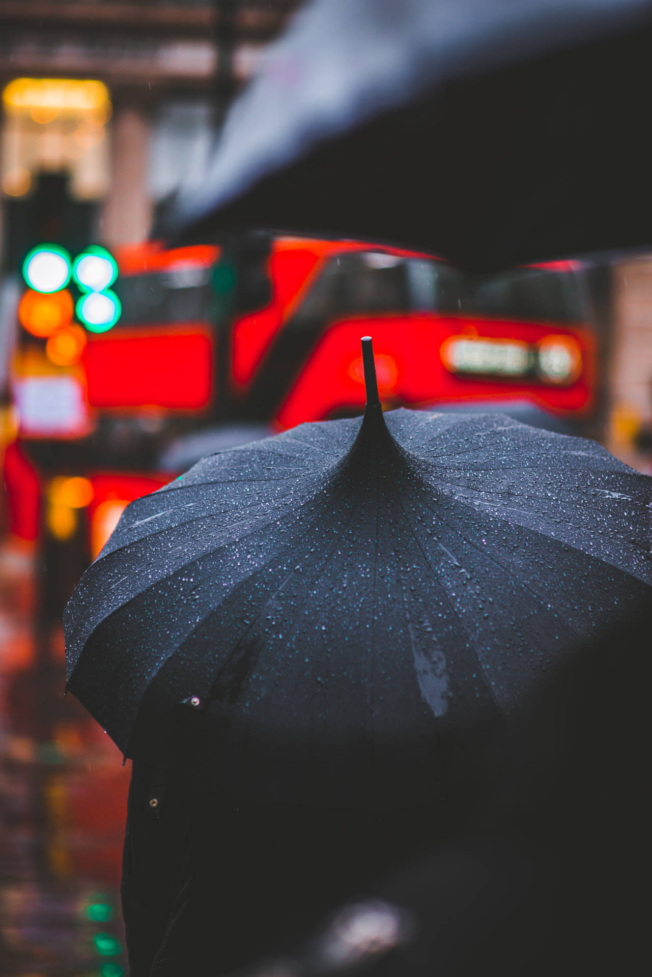 夜晚雨城中，一人手持黑色雨傘，周圍燈光閃爍。