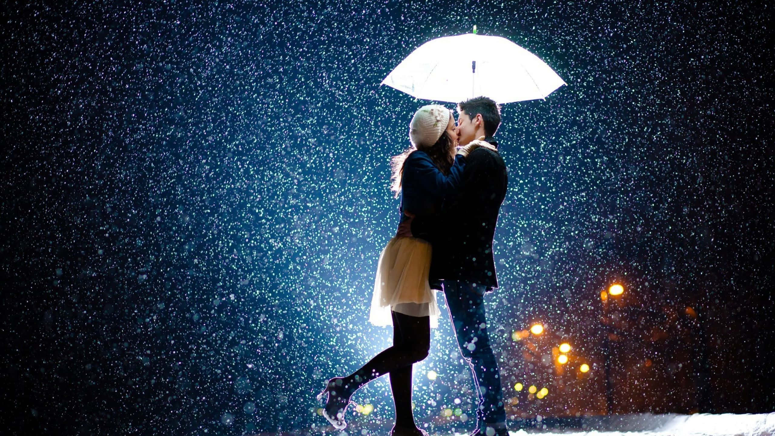 雨夜情侶共撐白傘畫面 壁紙 — 一對情侶在發光的白色雨傘下接吻，雪花飄落在漆黑的都市夜晚，溫暖的街燈照亮四周。