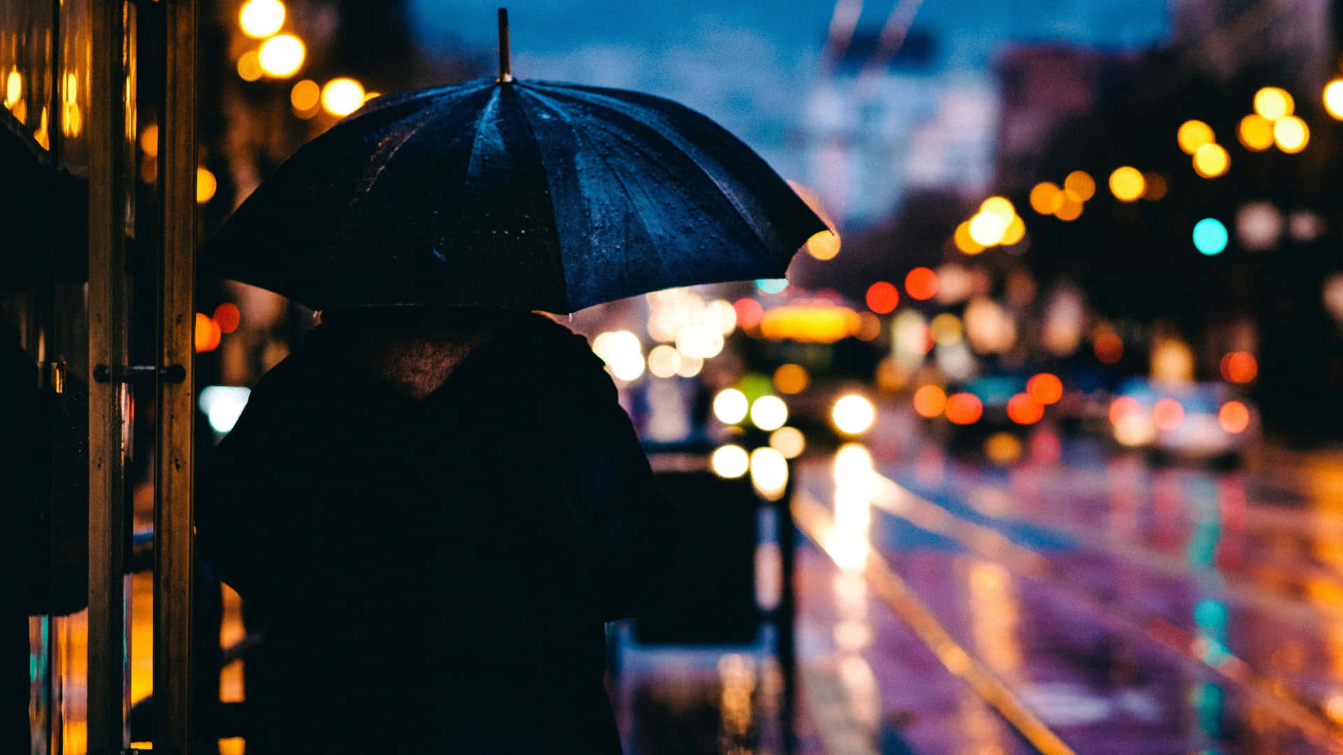 拿著黑色雨傘的人在雨夜的城市中行走，周圍有發光的燈光。