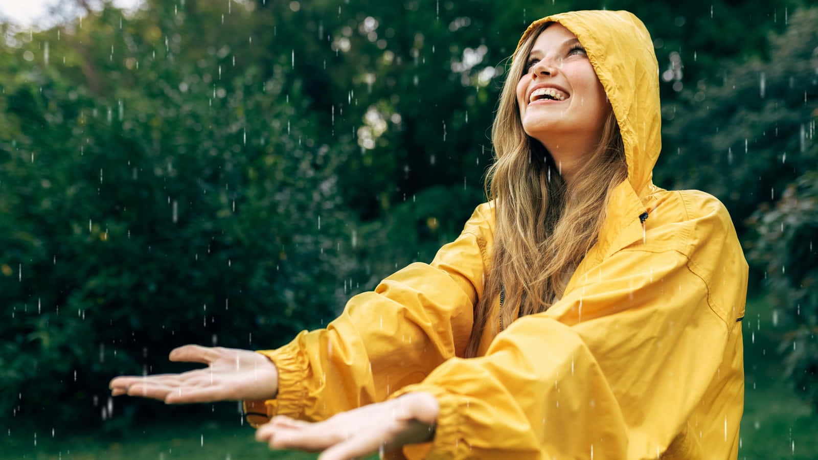 身穿黃色雨衣的女性在雨林中張開雙臂微笑