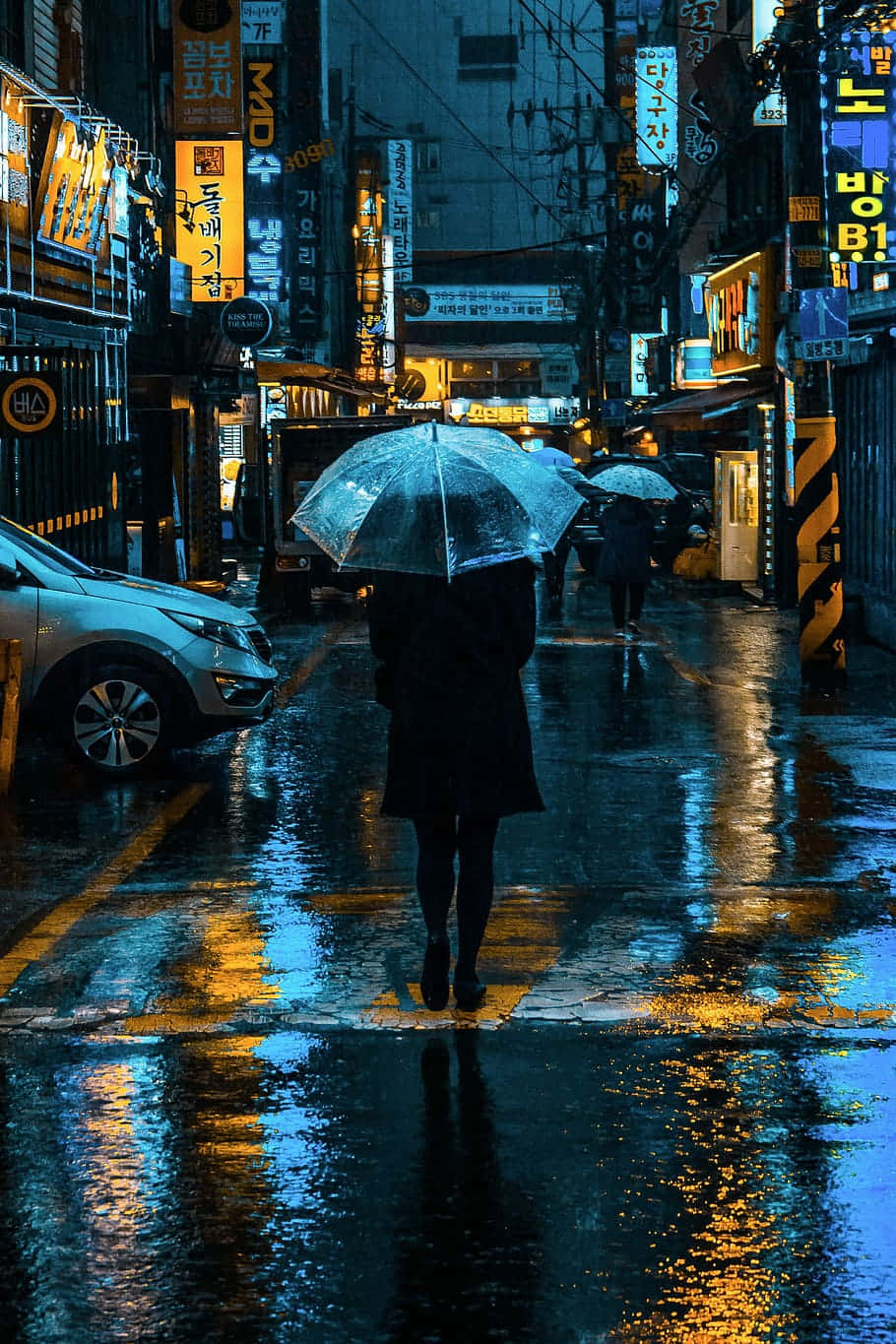 夜晚在雨中霓虹燈照亮的城市街道上，一個人獨自撐傘行走。