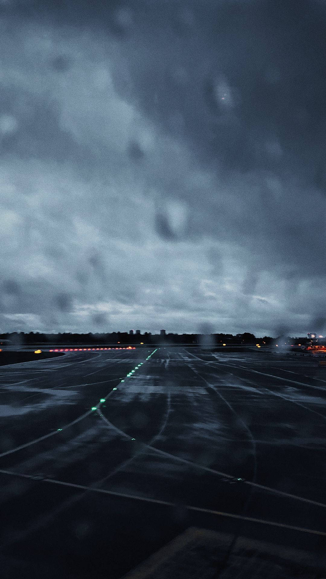 雨天跑道 壁紙 — 雨痕模糊了黑暗的機場停機坪，在暴風雨的天空下，跑道燈閃爍發光。