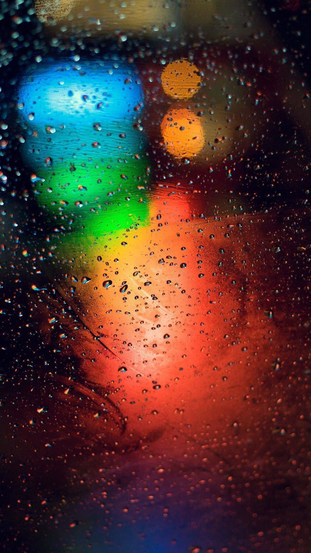 玻璃上的雨滴在夜間將多彩的城市燈光折射成模糊的散景。
