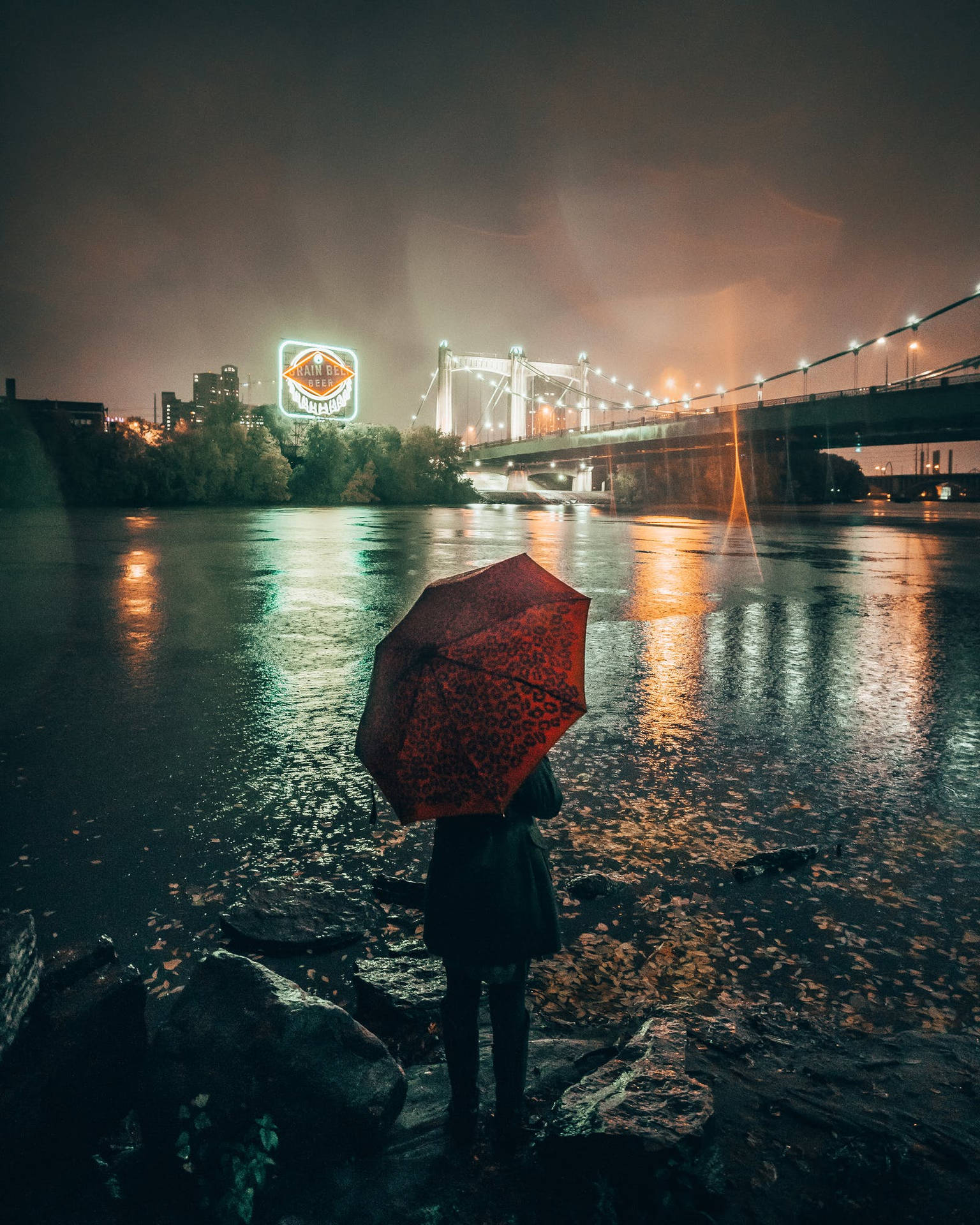 夜晚城市燈光下，河邊拿著紅色雨傘的人。