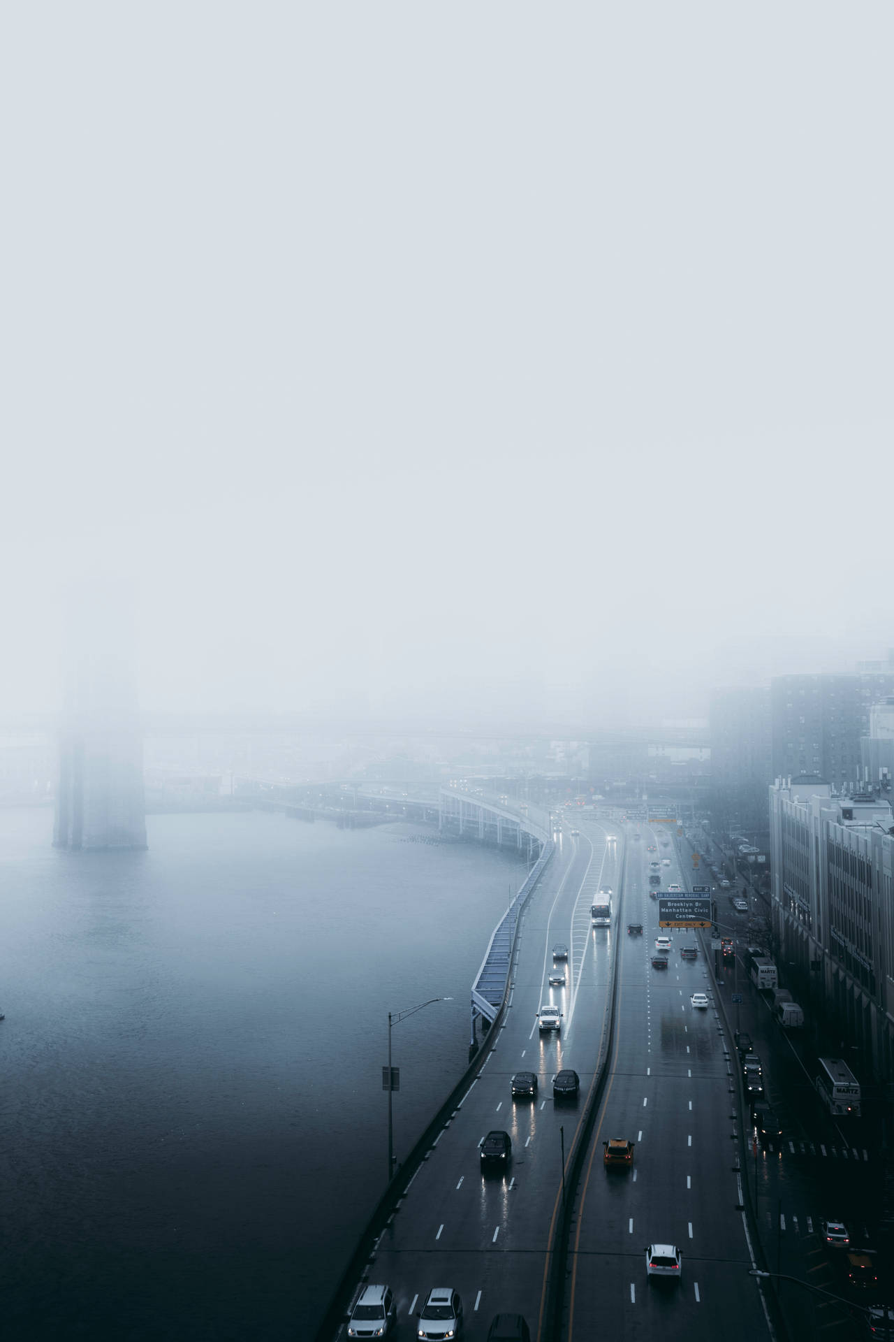 霧氣瀰漫的城市高速公路旁有水，遠處有建築物