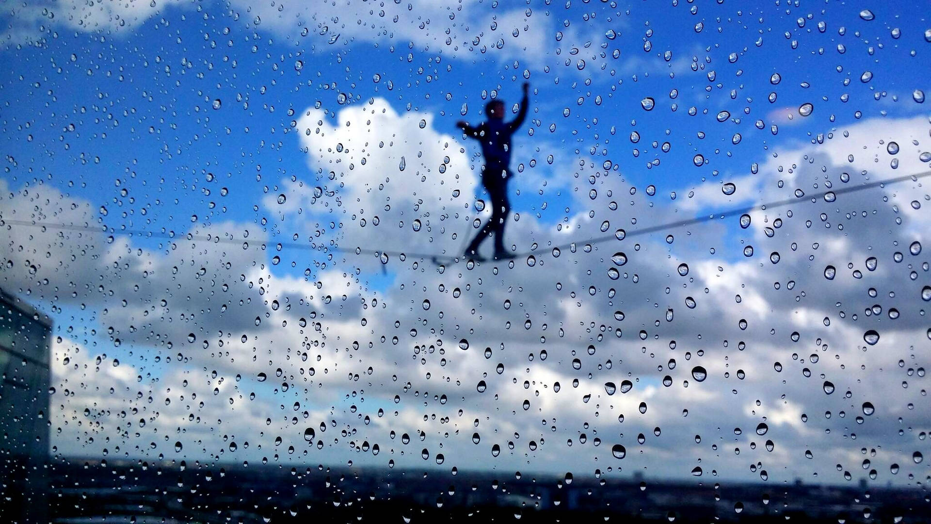 透過有雨痕的窗戶，看到一個人在鋼索上保持平衡。