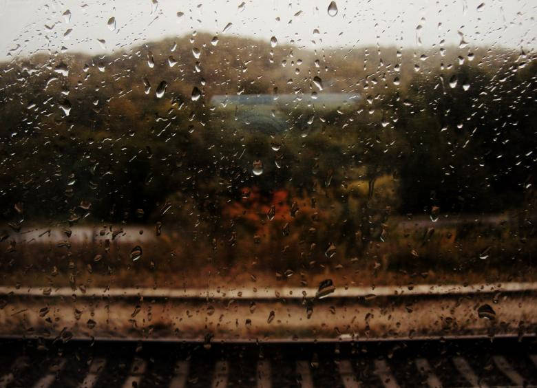 火車窗上的雨滴，顯示模糊的秋樹和軌道。