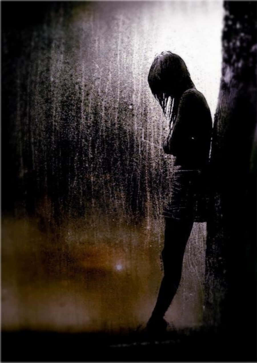 雨林中孤獨落淚的女孩 壁紙 — 一個孤獨的身影站在傾盆大雨中，靠著牆壁，在強烈的背光下低頭沉默。