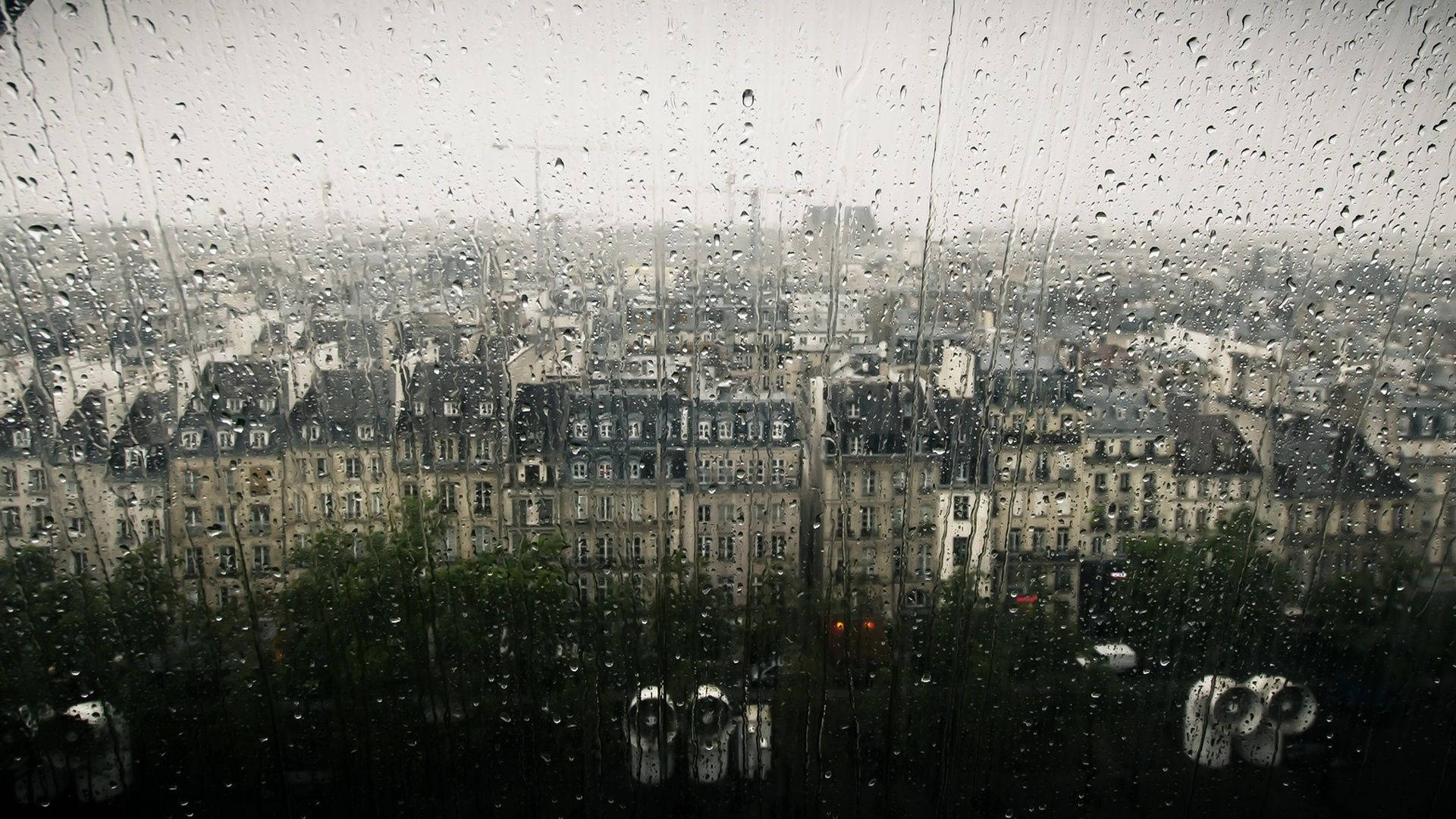 落雨 桌布 壁紙 — 雨水沿窗戶流下，顯露出灰色天空下歐式建築的迷濛城市天際線。