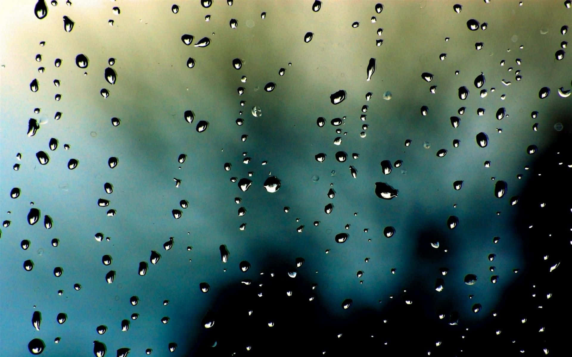 落雨 桌布 壁紙 — 雨滴依附在玻璃窗上，顯露出窗外模糊的藍綠色和灰色天空。