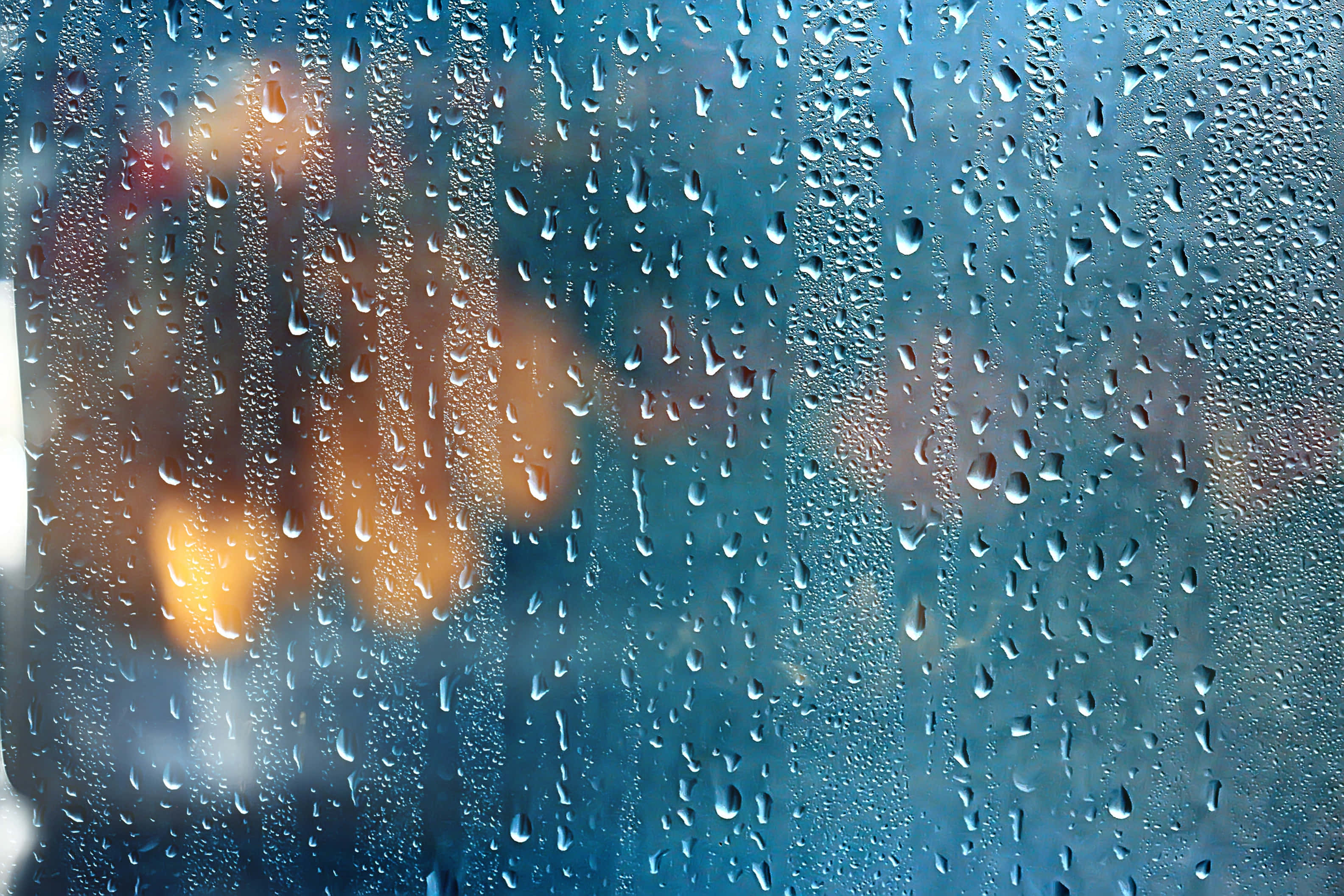 Rainy Day 桌布 壁紙 — 雨滴依附在窗戶上，顯露出外面模糊的暖色燈光，帶有冷藍色調。