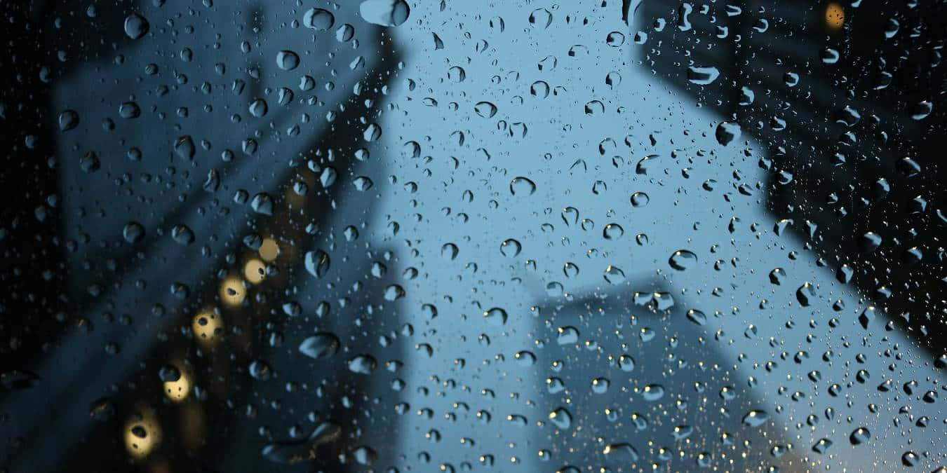 天氣 桌布 壁紙 — 雨滴依附在窗戶上，顯露出暮色中模糊的城市燈光和黑暗的建築物。
