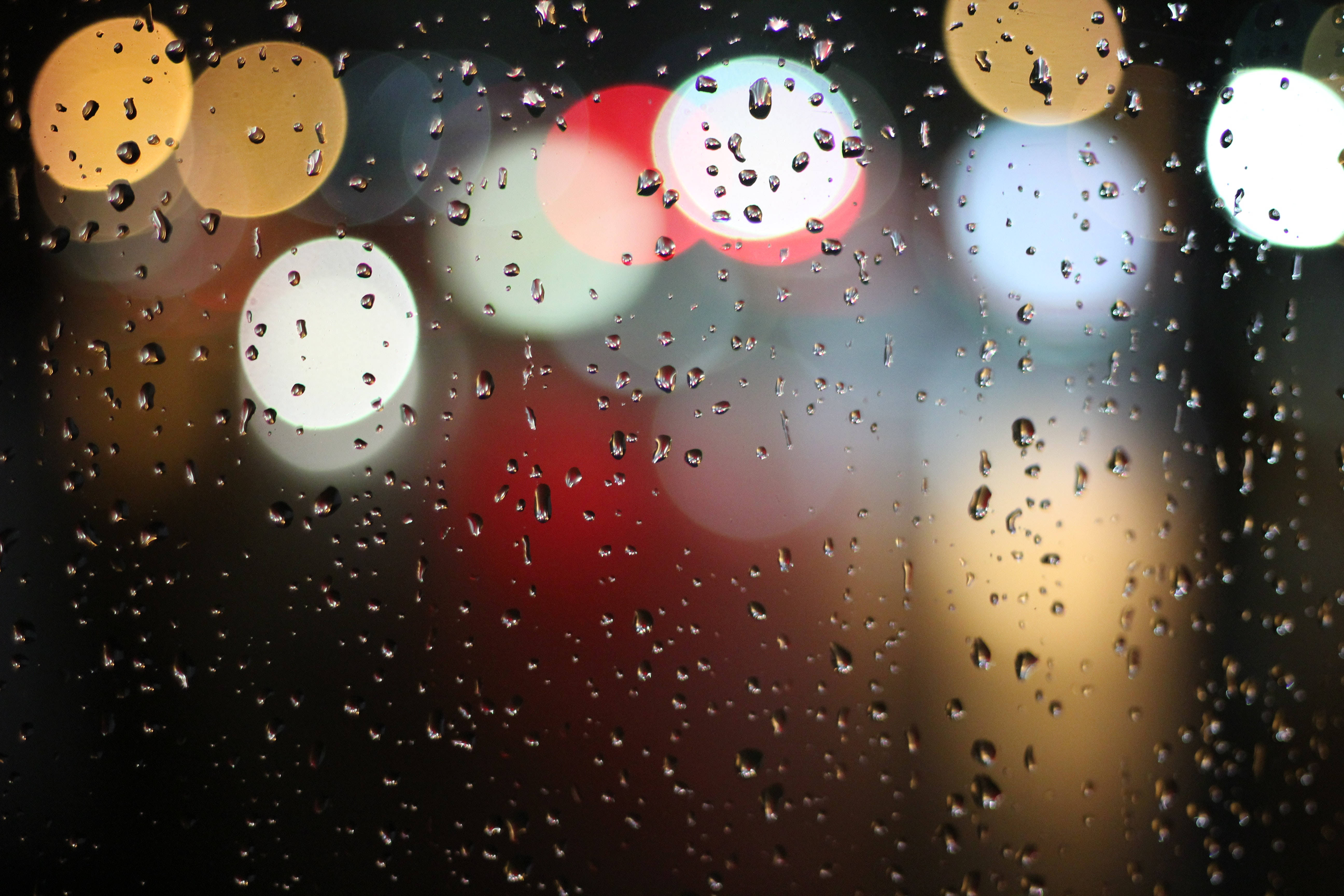 鎖屏 桌布 壁紙 — 雨滴依附在窗戶上，顯露出模糊的城市燈光，在溫暖的紅色、黃色和白色中閃耀，映襯著漆黑的夜晚。