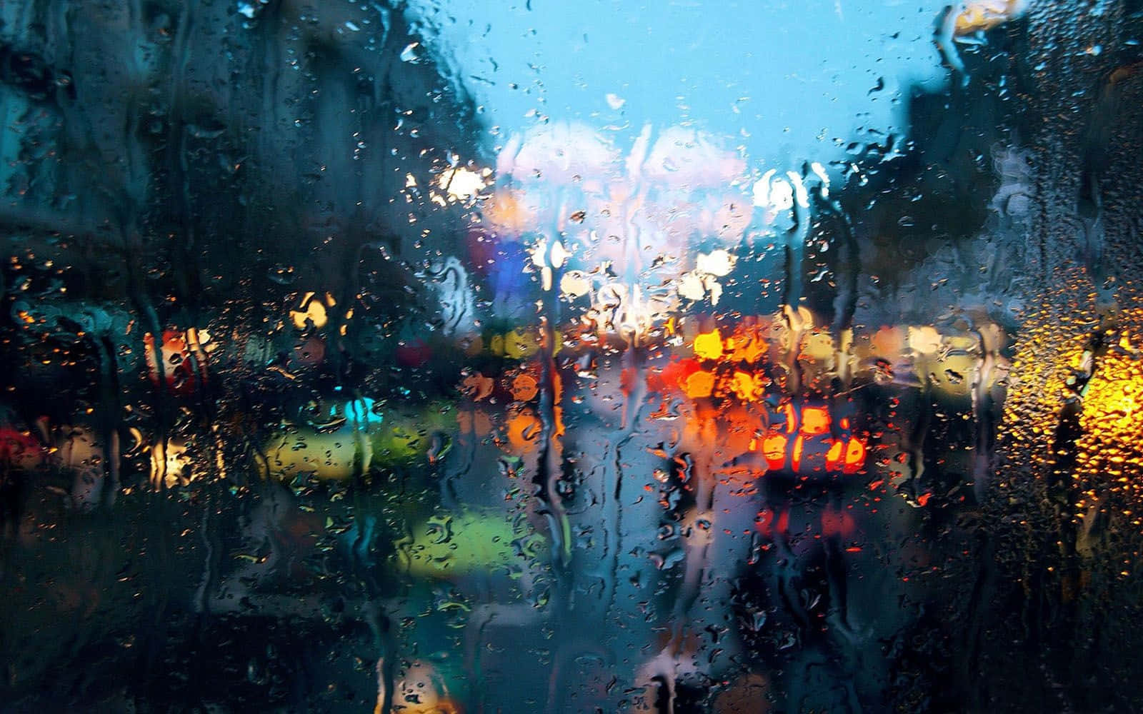 落雨 桌布 壁紙 — 雨滴劃過車窗，將充滿活力的城市燈光模糊成發光的抽象條紋，映襯著涼爽的藍色暮色。