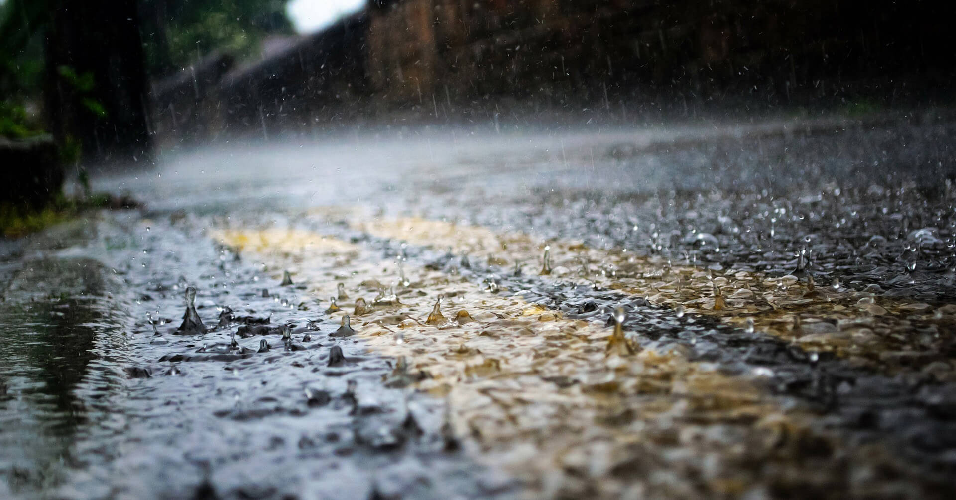 落雨 桌布 壁紙 — 雨滴在濕漉漉的瀝青路上飛濺並泛起漣漪，反射出模糊背景中柔和的金色光芒。