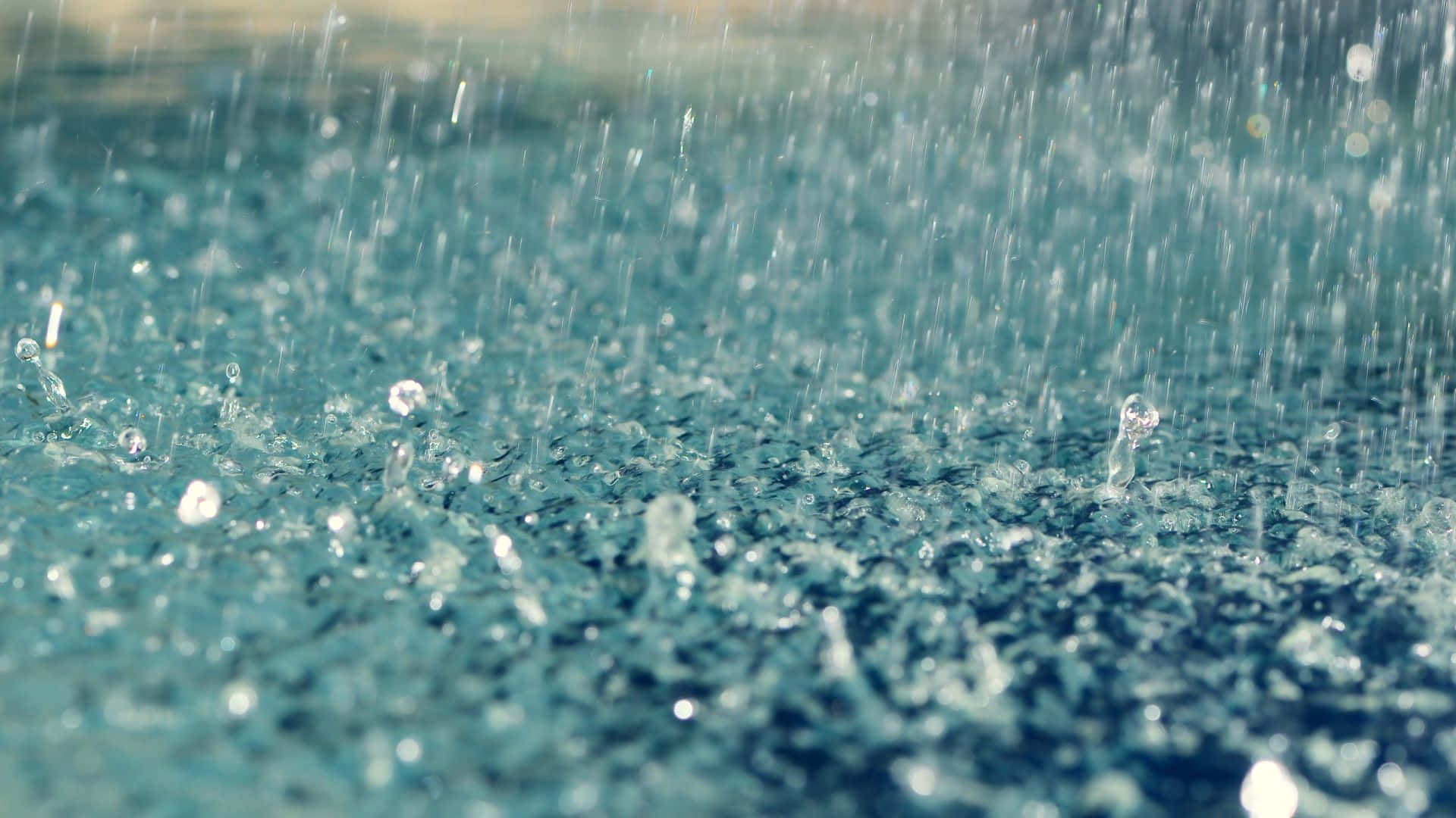 Raining 桌布 壁紙 — 雨滴在青綠色的水面上飛濺並泛起漣漪，形成閃閃發光的水珠和溫柔的波浪。
