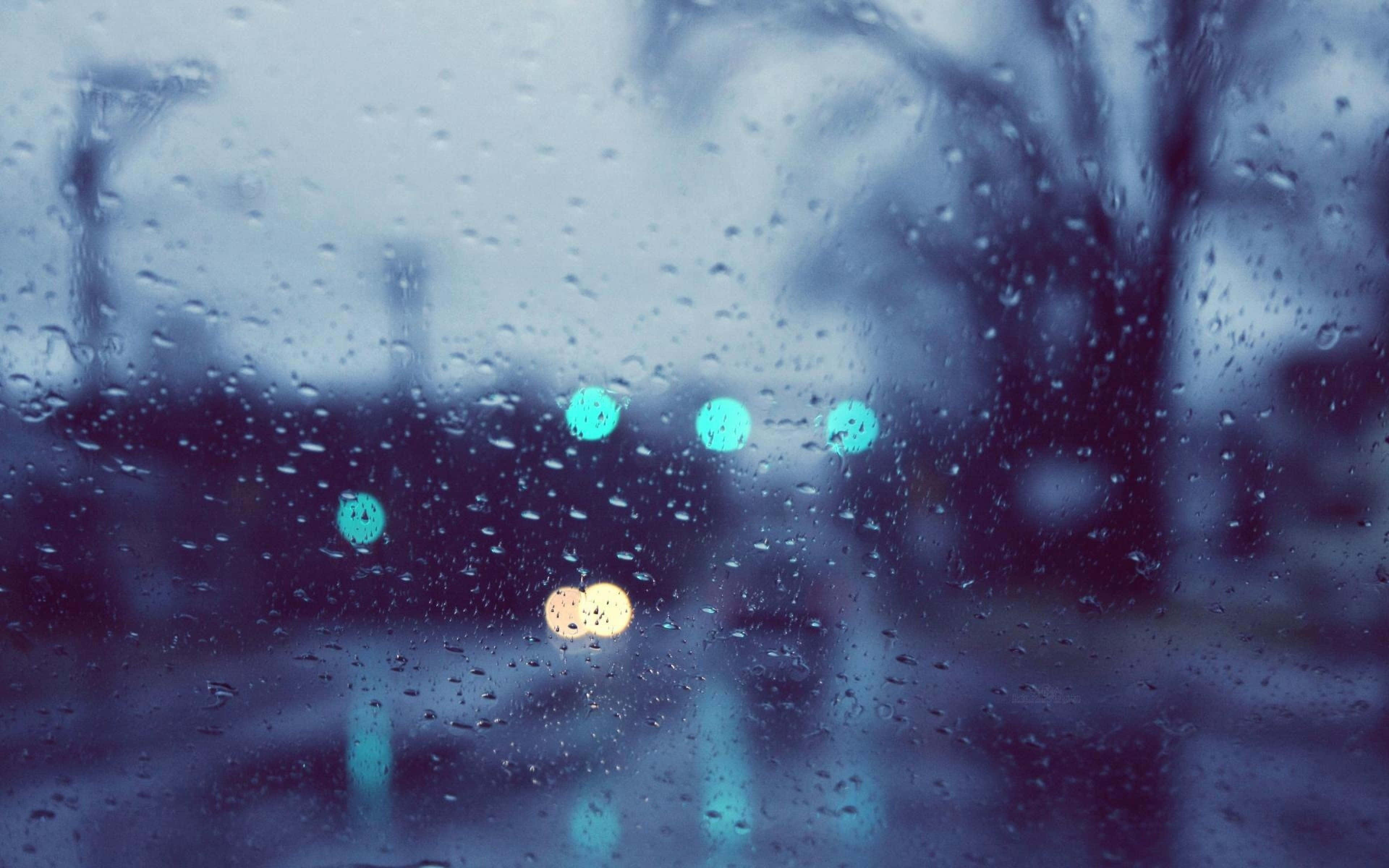 落雨 桌布 壁紙 — 雨滴模糊了窗外的景色，發光的青綠色和琥珀色燈光在雨中的城市場景中掠過。