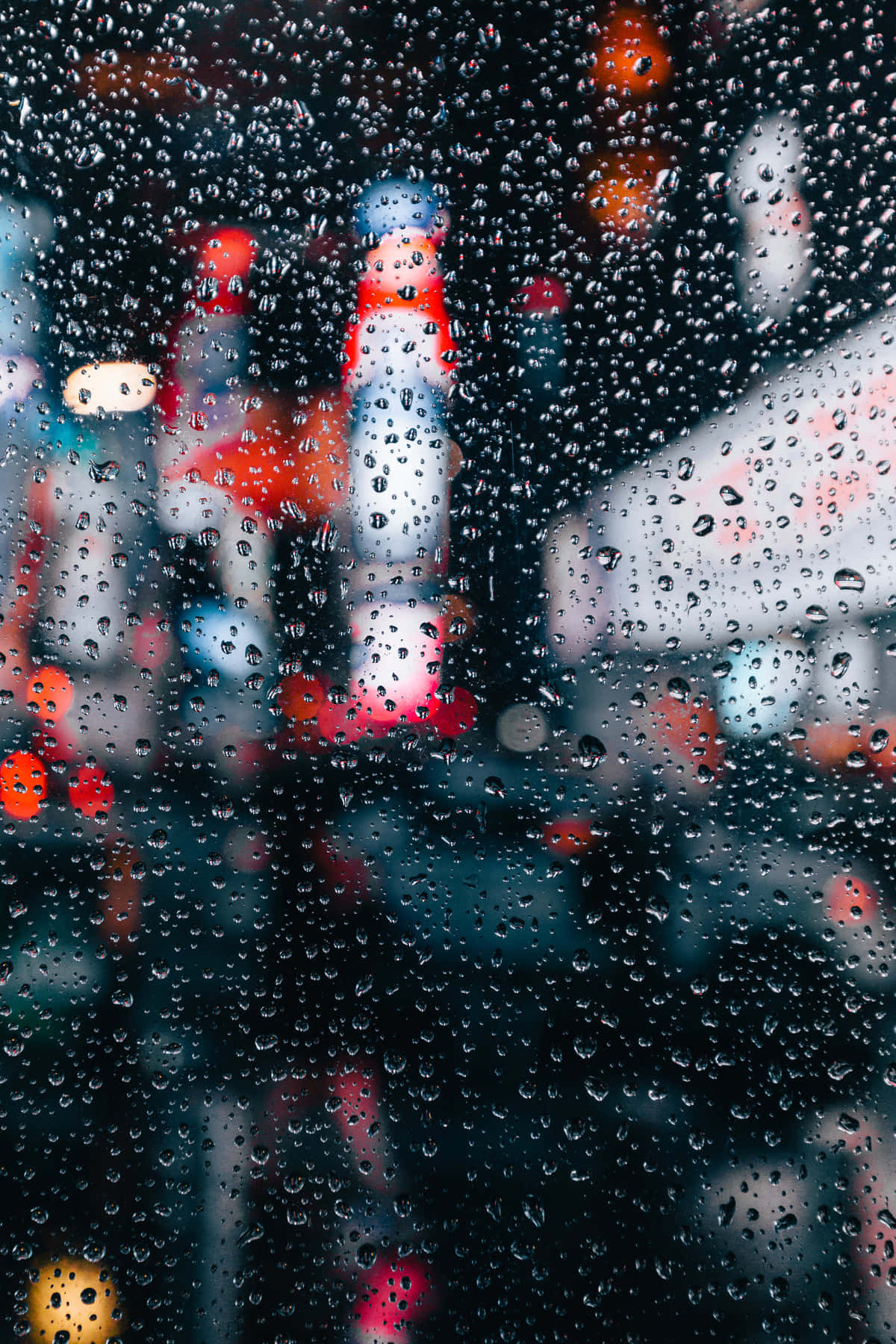 雨滴模糊夜景人像冷調照片背景 壁紙 — 雨滴透過夜晚的濕窗，將充滿活力的城市燈光模糊成發光散景。