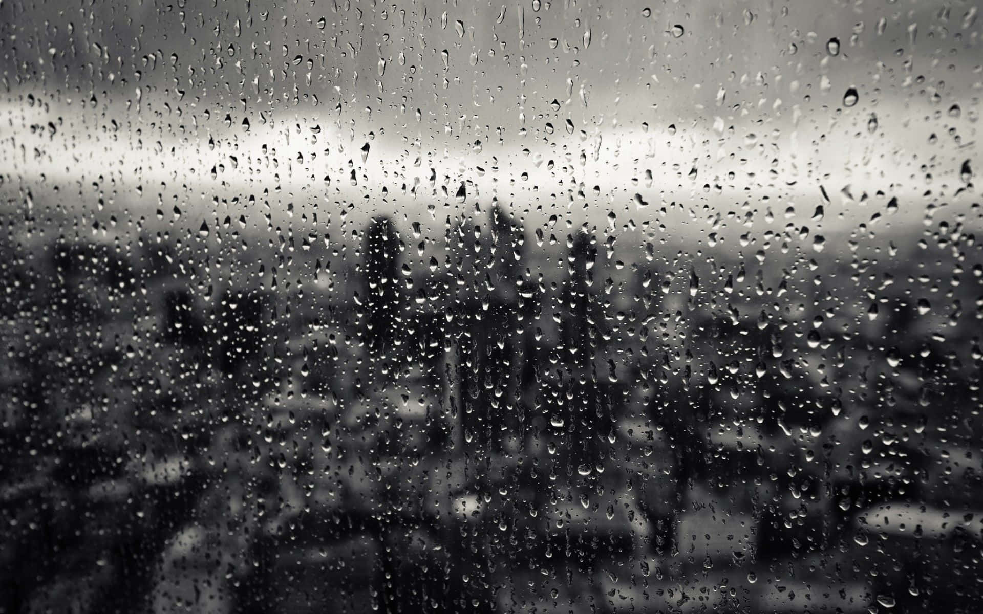 Raining 桌布 壁紙 — 雨滴沿玻璃窗流下，將單色城市景觀模糊成柔和剪影。