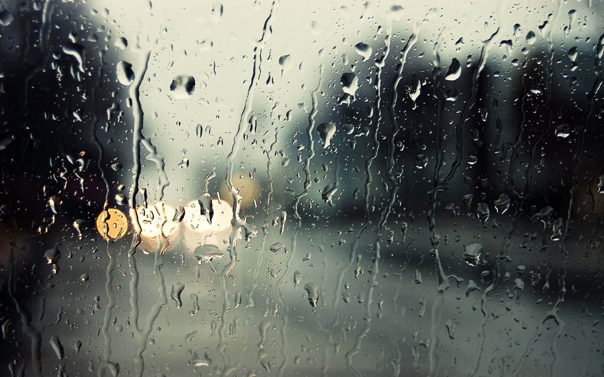 Raining 桌布 壁紙 — 雨滴沿著車窗流下，將城市燈光模糊成柔和發光的光球，映襯在灰色背景上。