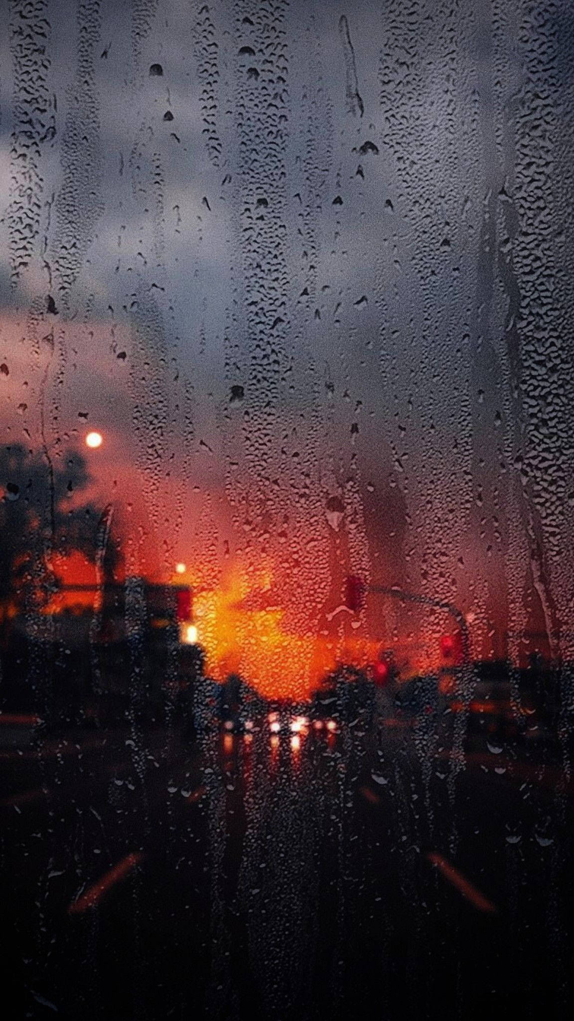 落雨 桌布 壁紙 — 雨滴沿著車窗流下，熾熱的橙色夕陽光線透過濕玻璃變得模糊。