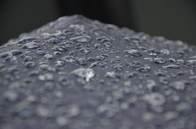 在柔焦中，深色紋理表面上的閃爍雨滴。