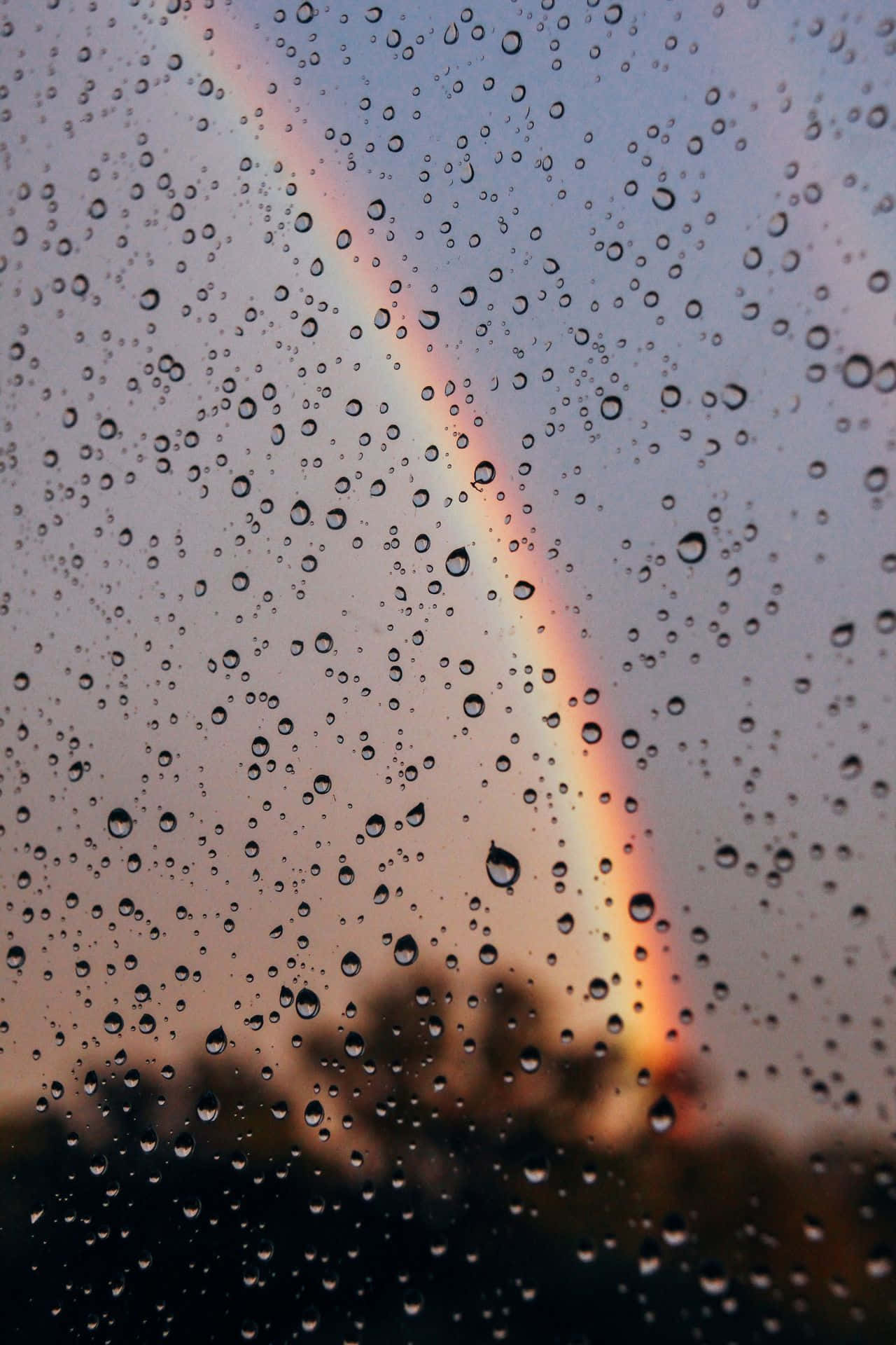 玻璃上的雨滴框住了暮色天空中的彩虹