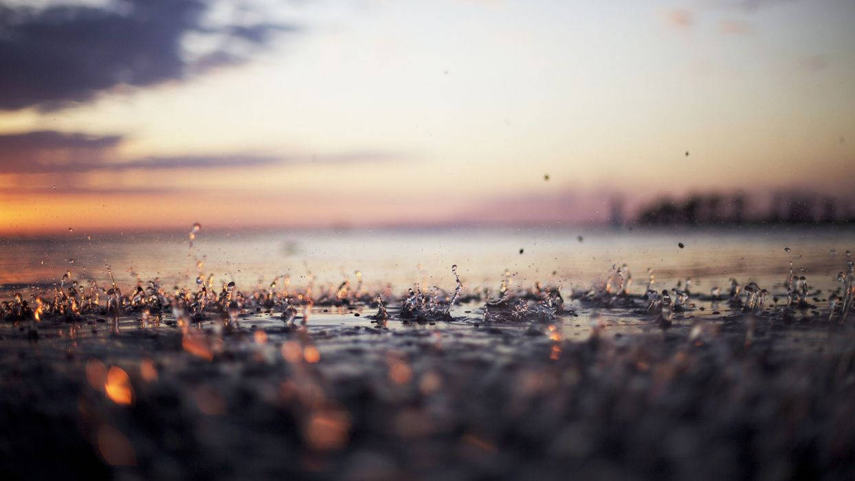 金色夕陽與紫色雲朵下，雨滴濺在濕地上