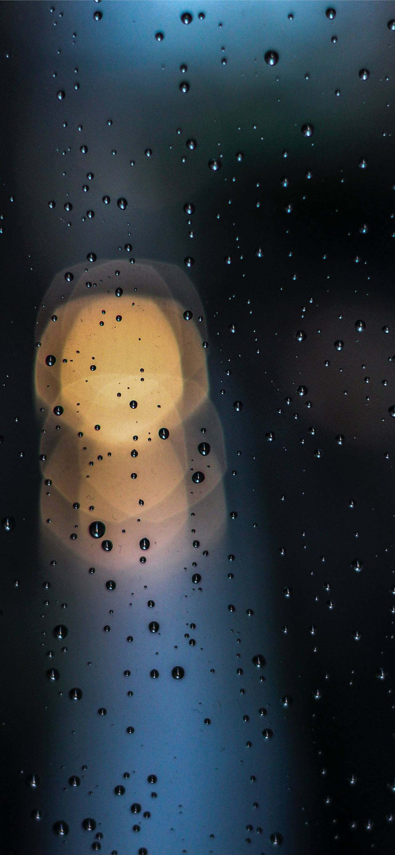 Bokeh 桌布 壁紙 — 雨滴附在窗戶上，映出模糊的暖光，背景是清涼的藍色夜空。