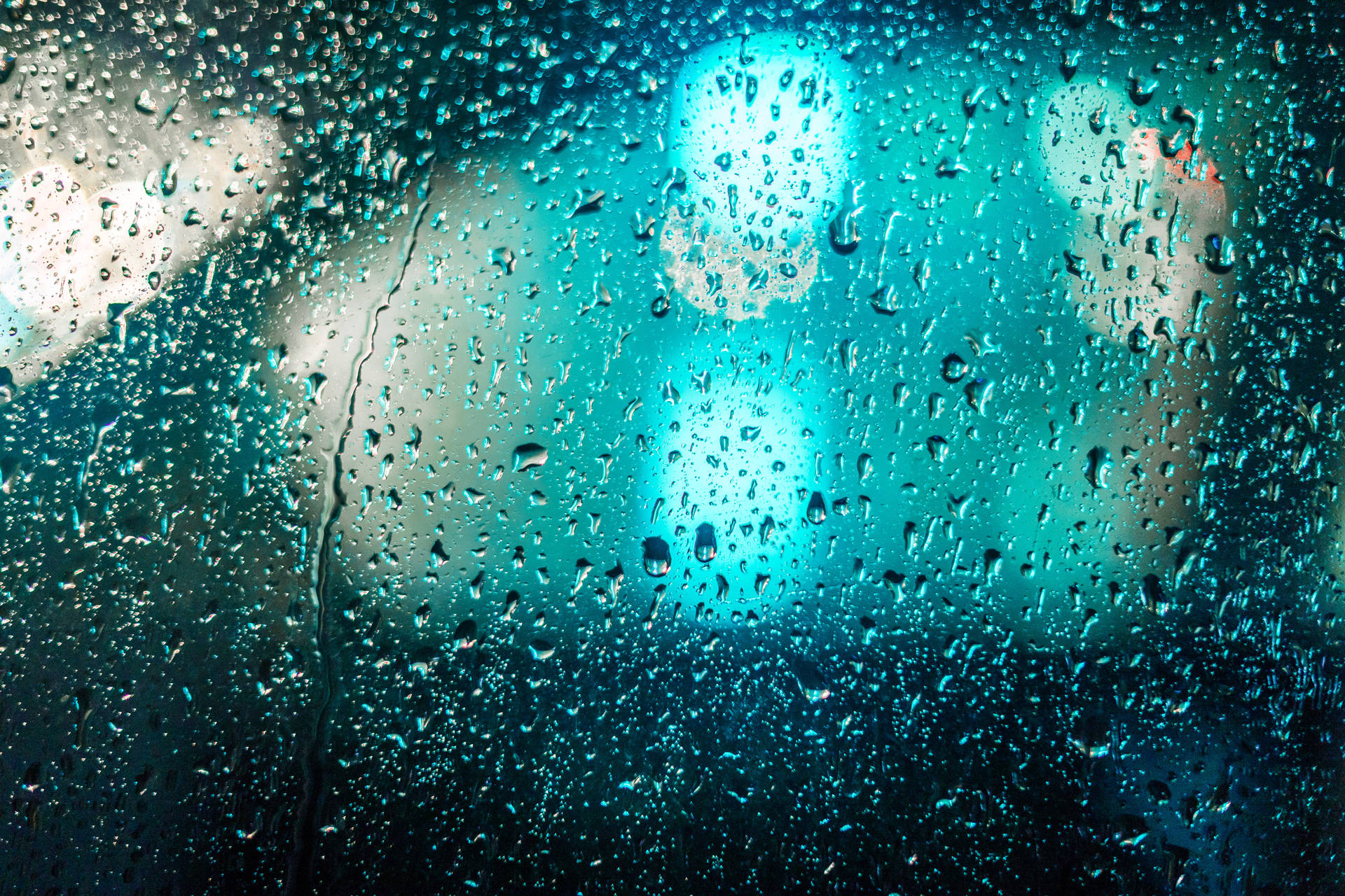 窗戶上的雨滴，夜晚模糊的藍綠色城市燈光。