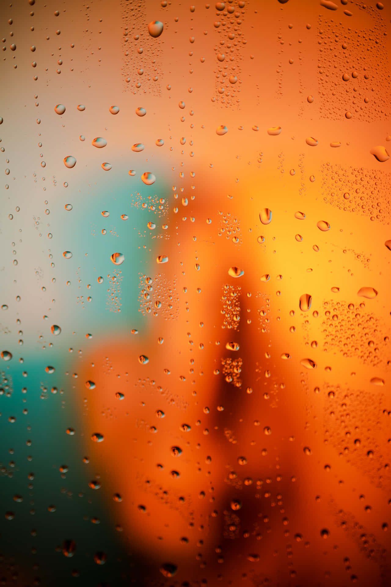 黃昏時窗戶上的雨滴，模糊的橙色和藍綠色城市燈光。