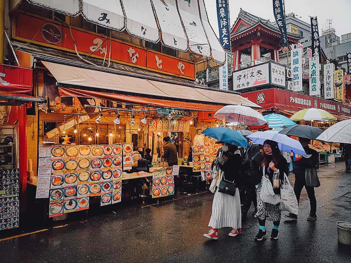 Street 桌布 壁紙 — 雨濕的東京街道，行人撐傘經過充滿活力的美食攤檔和傳統紅色招牌。