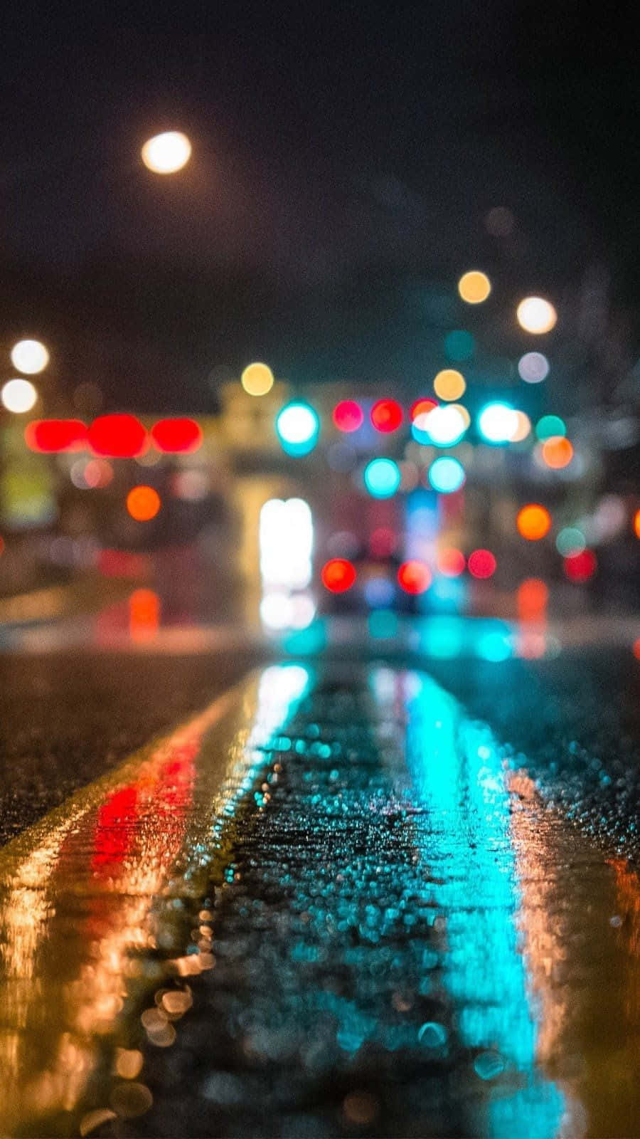 Smartphone 桌布 壁紙 — 雨濕的都市街道在夜晚反射來自交通和街燈的發光散景燈光。